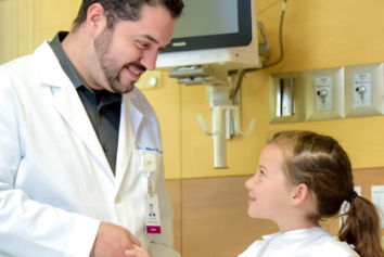 Médico sonriente estrechando manos con una niña que goza de salud Médico sonriente estrechando manos con una niña que goza de salud