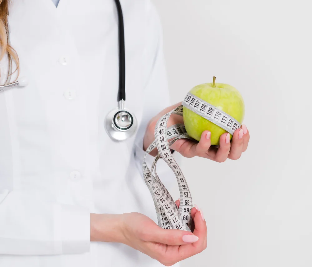 Una doctora sostiene una manzana y una cinta métrica, ilustrando la labor de los nutriólogos bariátras en el control del peso. Una doctora sostiene una manzana y una cinta métrica, ilustrando la labor de los nutriólogos bariátras en el control del peso.