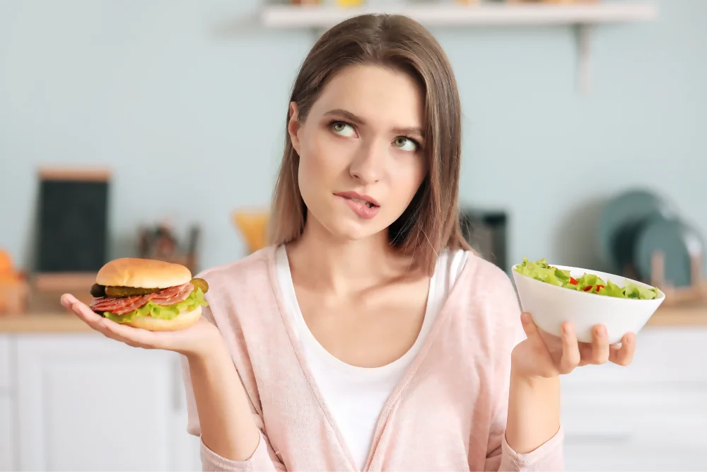 Una mujer joven se debate entre optar por una alimentación saludable con el nutricionista o darse un gusto con una hamburguesa. Una mujer joven se debate entre optar por una alimentación saludable con el nutricionista o darse un gusto con una hamburguesa.