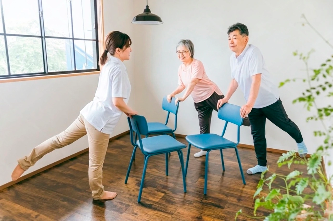 Especialista enseñando a adultos mayores cómo hacer ejercicio desde casa, sin equipo especial, usando sólo unas sillas.
